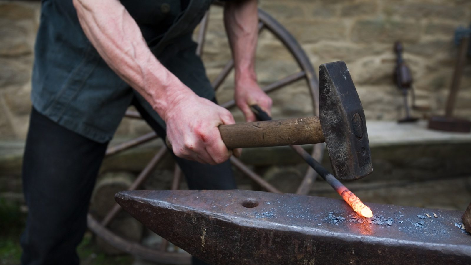 Blacksmith forge workshop interior with anvil, hearth, and hand tools on the wall