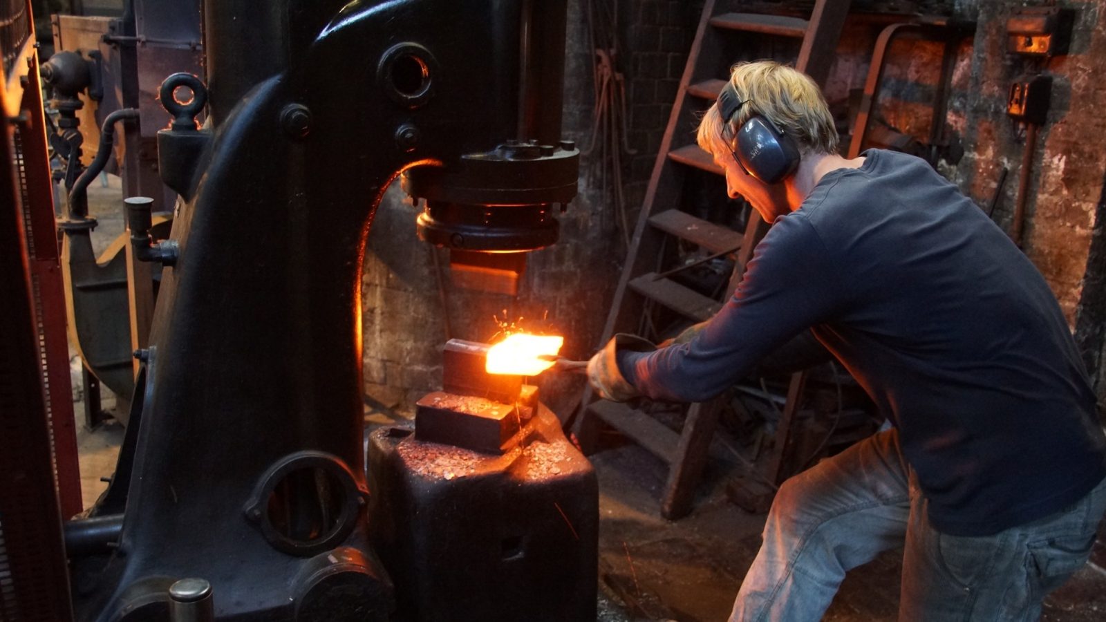 Blacksmith hammering a glowing steel billet under a power hammer