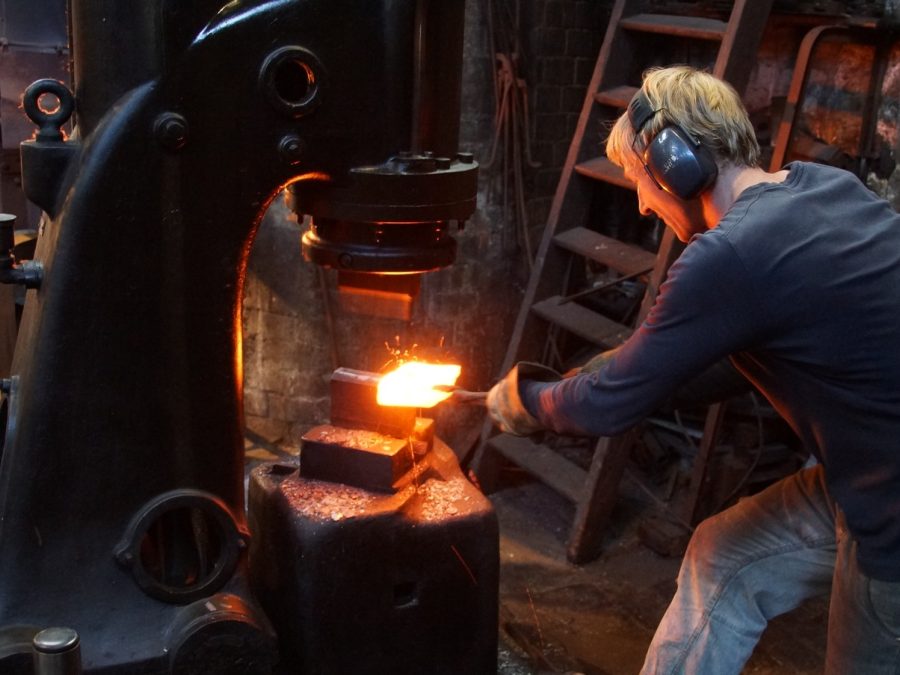 Blacksmith hammering a glowing steel billet under a power hammer