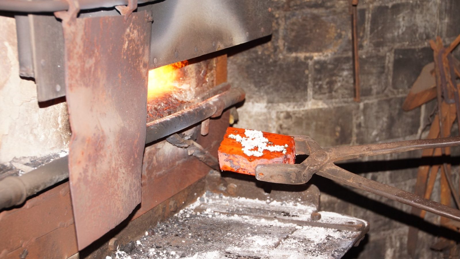 Smith drawing a glowing hot steel billet from the forge fire