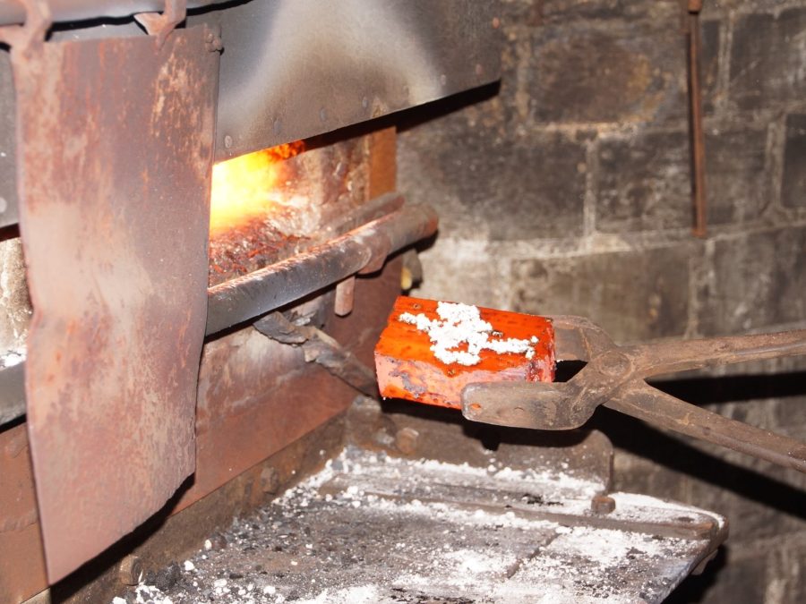 Smith drawing a glowing hot steel billet from the forge fire