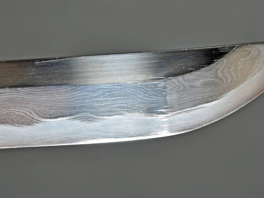 Polished carbon steel blade tip showing a visible hamon temper line
